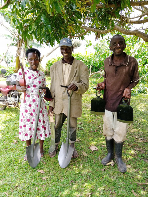 Three people smile holding pit latrine tools